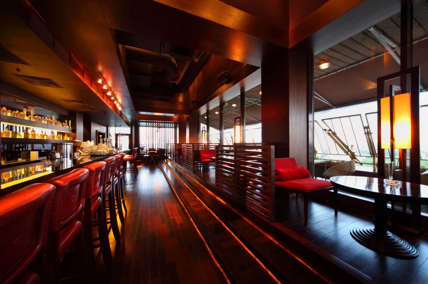 A long wooden table with red chairs in front of windows.