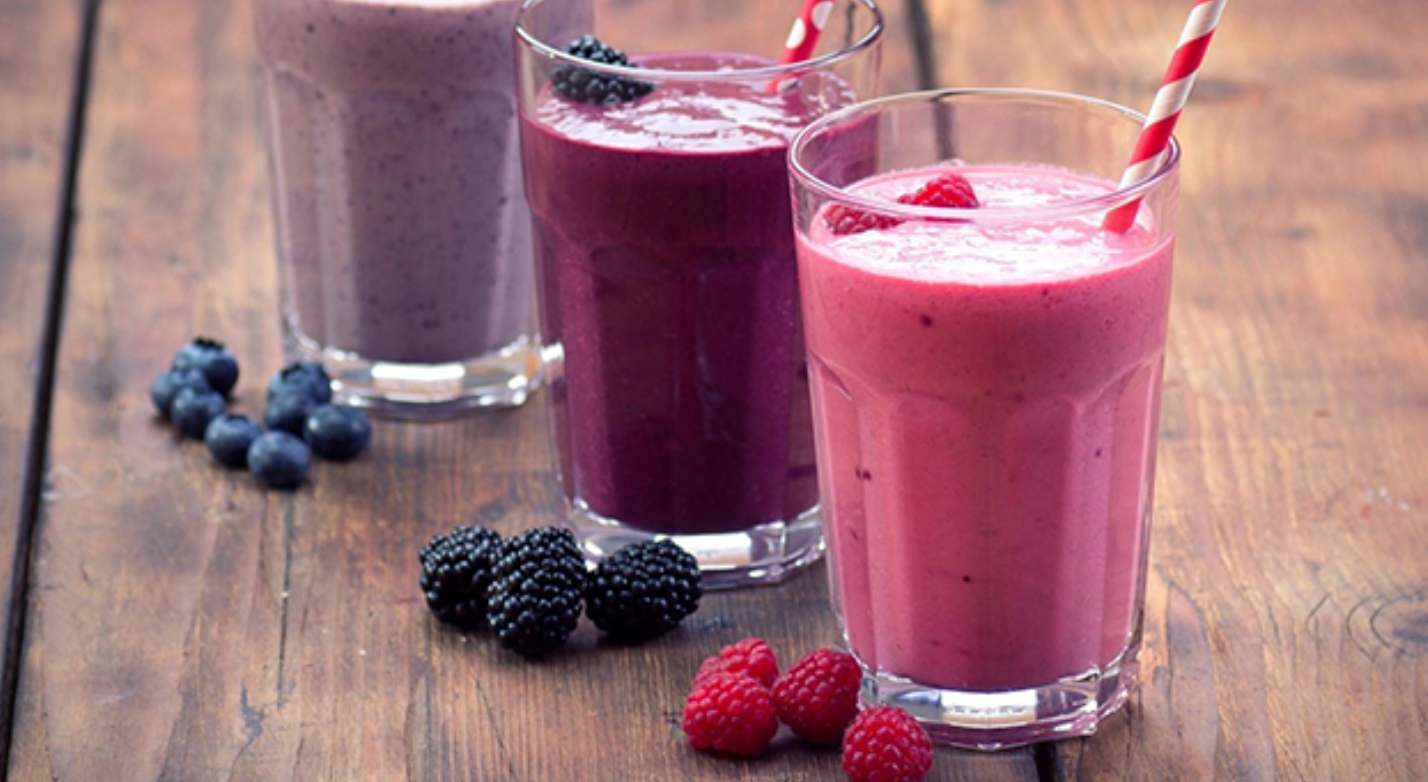 Three glasses of smoothies are sitting on a table.