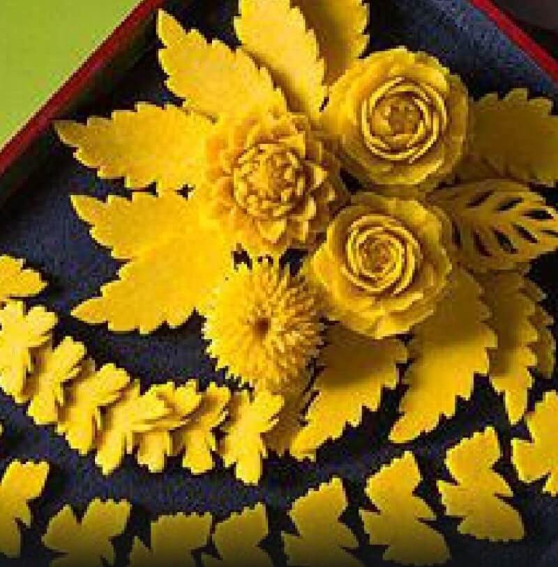 A yellow flower arrangement with roses and leaves.