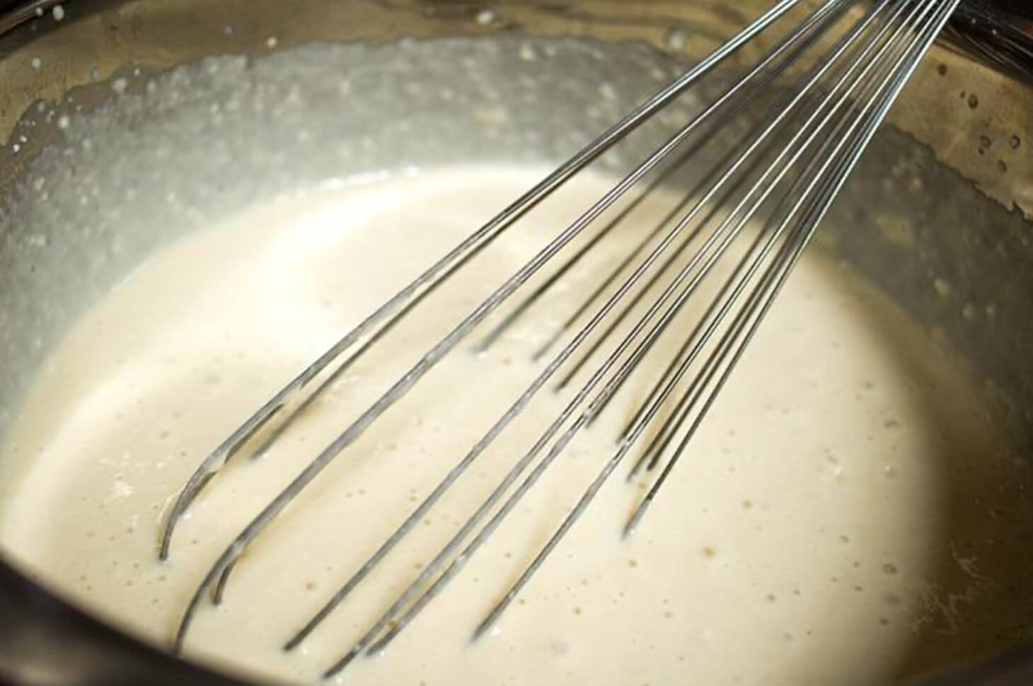 A bunch of whisks in a pan with some liquid