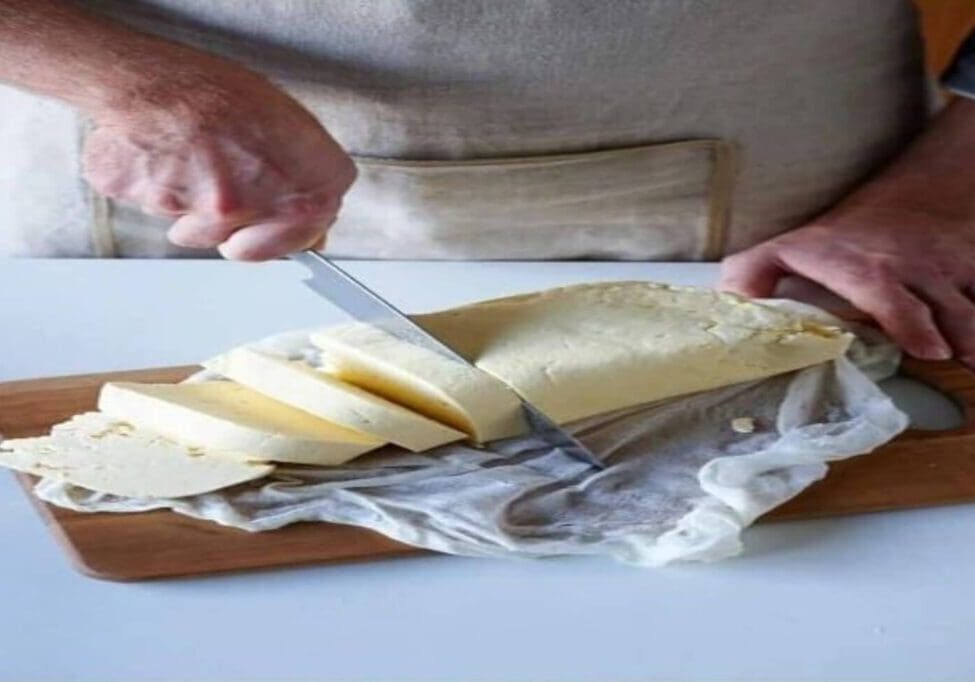 A person slicing cheese on top of a cutting board.